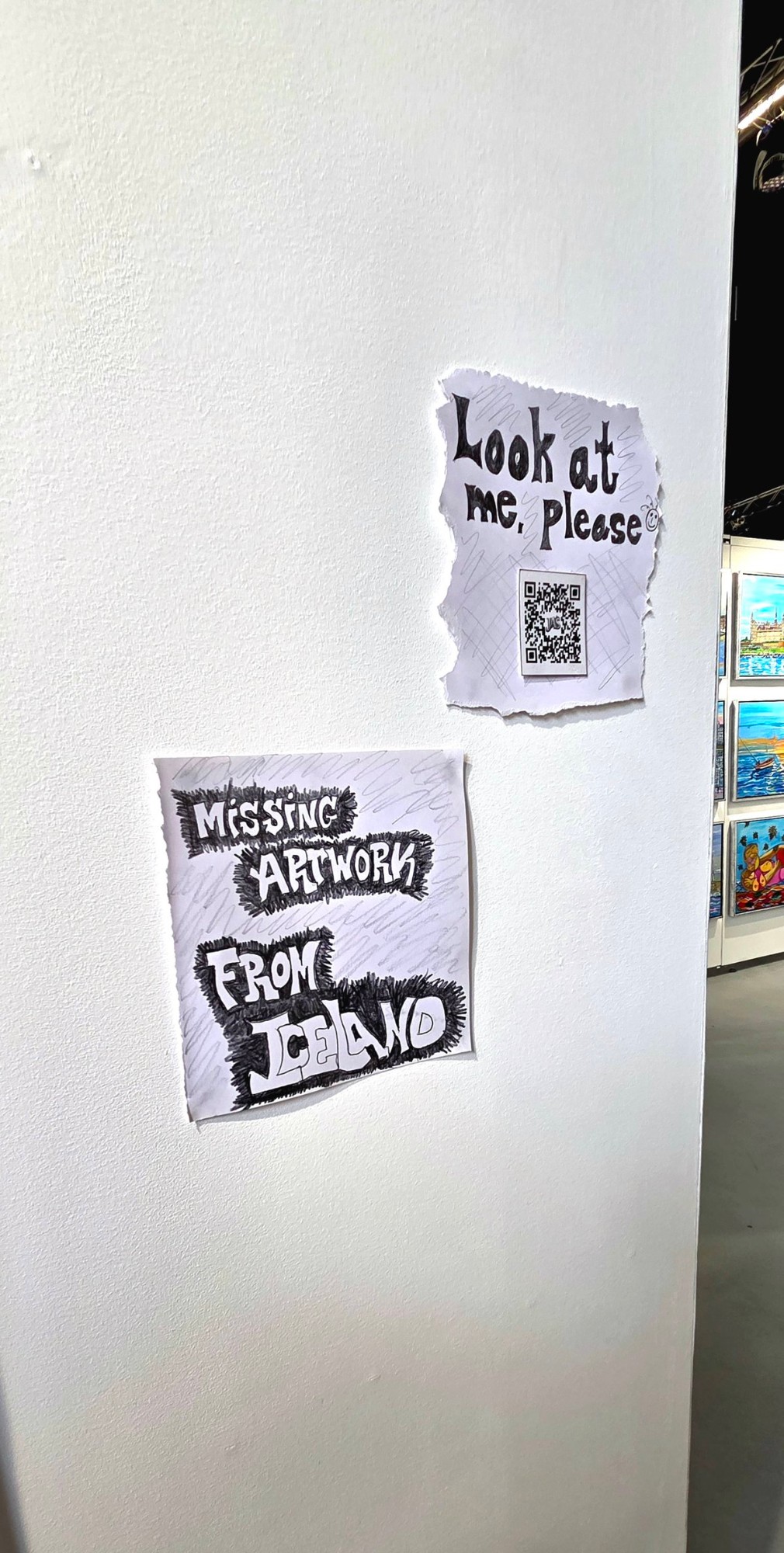 Hand-drawn signs on the booth wall at Art Nordic reading “Missing artwork from Iceland” and “Look at me, please” with a QR code